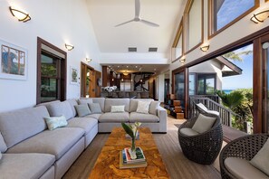 Un amplio salón con un sofá modular grande, una mesita de centro con libros, sillones de mimbre y vistas al exterior.