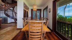 Een eetgedeelte met een houten tafel en stoelen, een spiltrap en een groot raam met uitzicht op de oceaan.
