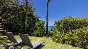 Een tuin met loungezetels, een palmboom en uitzicht op de oceaan.