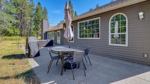A patio with a table and chairs, a covered grill, and a house with large windows. - Riffle Road Ranch: 10 Acres, 8 Mi to Silverwood (Spirit Lake)