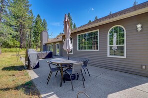 Eine Terrasse mit Tisch und Stühlen, ein überdachter Grill und ein Haus mit großen Fenstern.