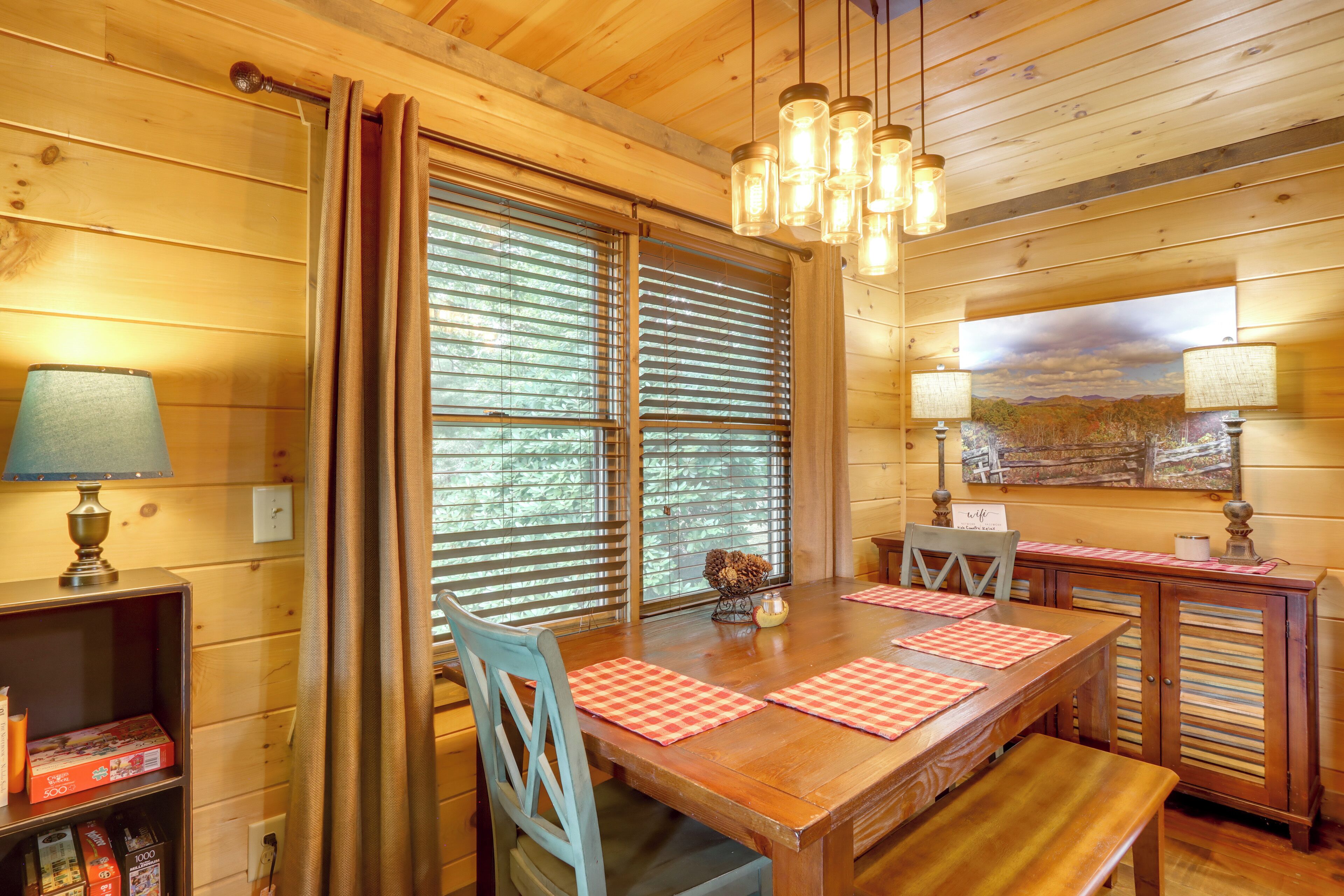 A wooden interior with a dining table, chairs, a bench, a lamp, and a window with blinds.