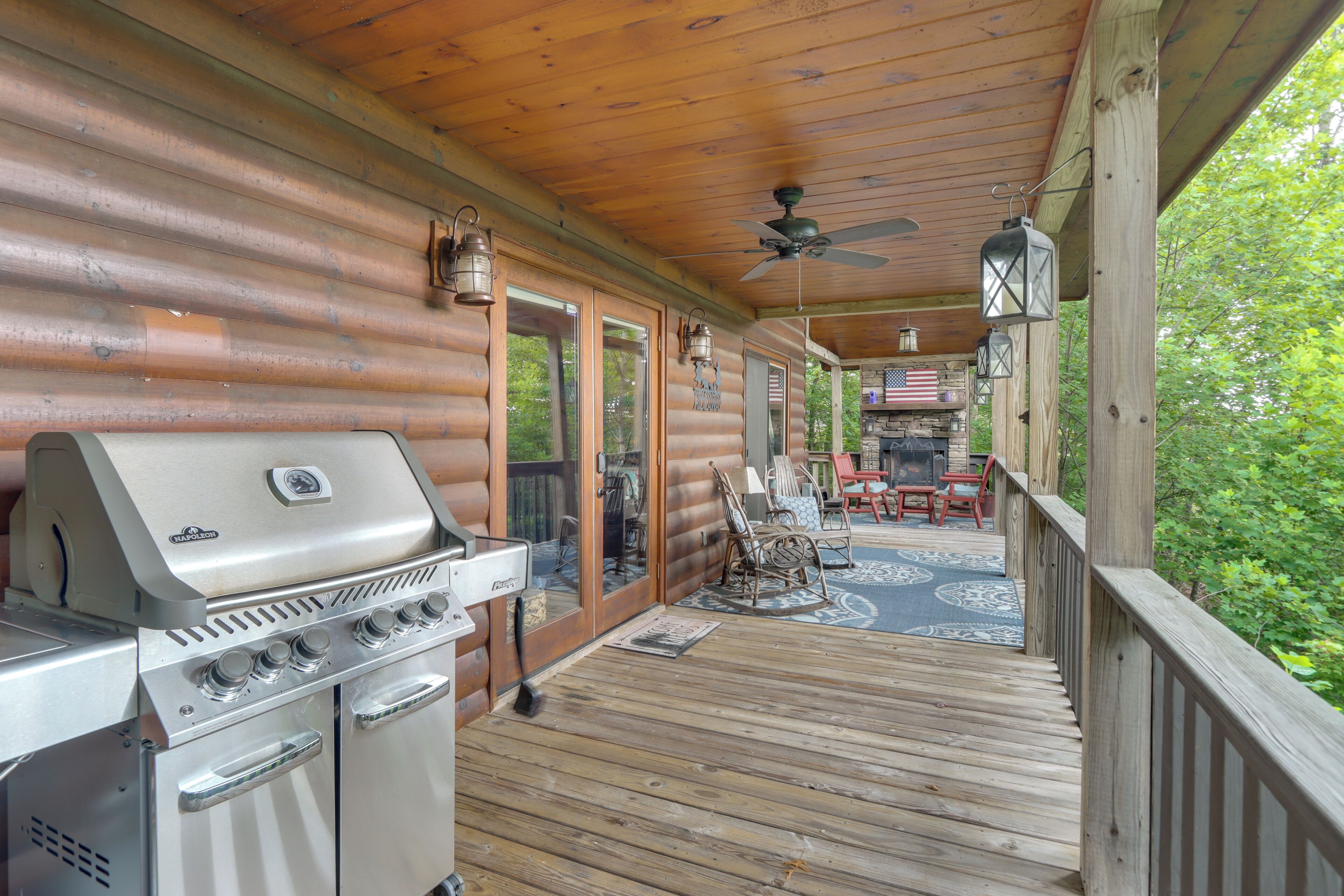 A covered deck with a grill, outdoor furniture, and a view of the surrounding forest.