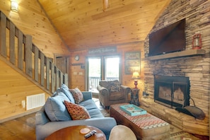 A cozy cabin interior with a wooden staircase, a fireplace, a sofa, and a television. - Blue Ridge Bliss: Peaceful Retreat w/ Deck (Blue Ridge)