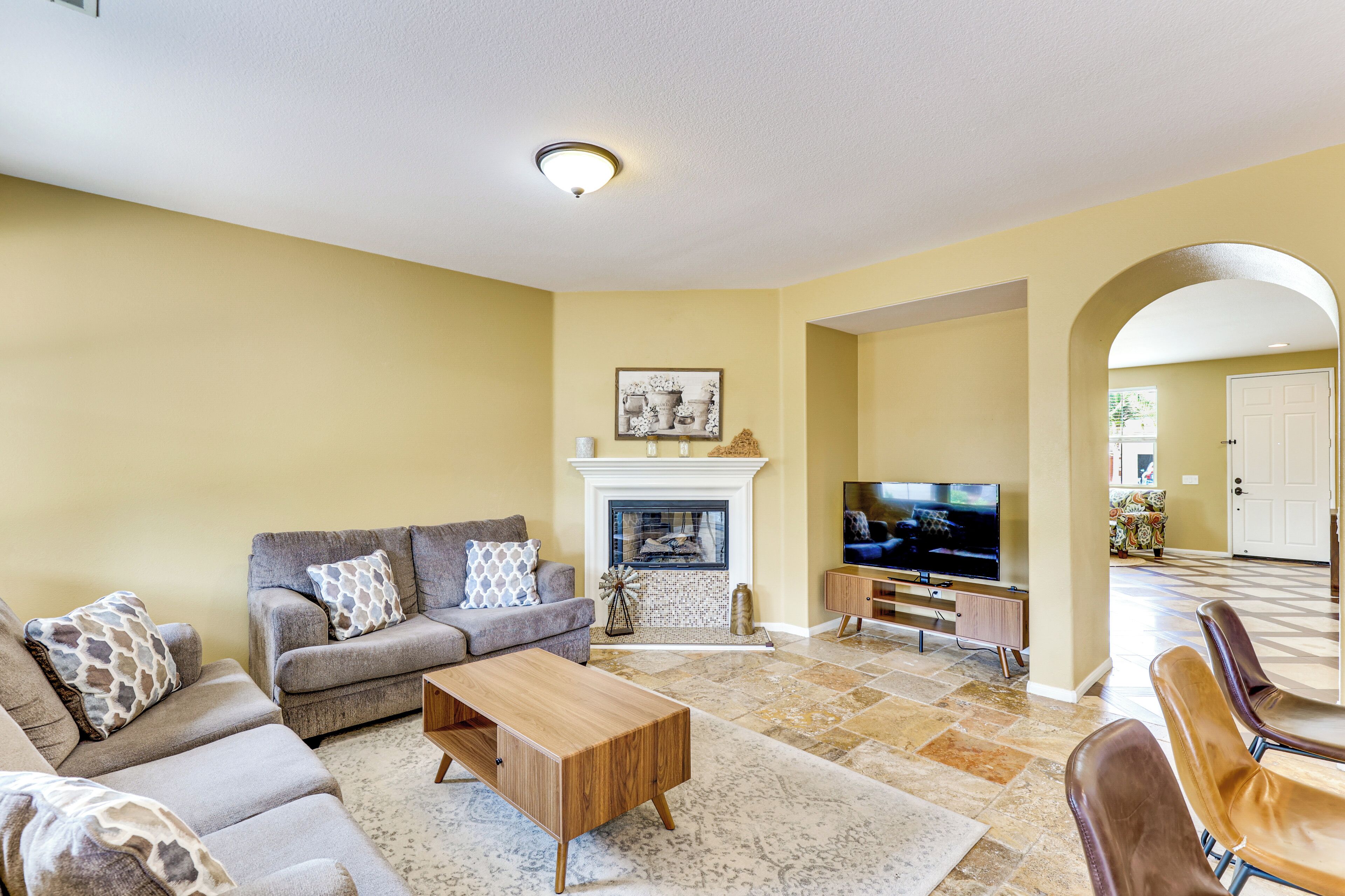 A living room with a sofa, coffee table, fireplace, TV, and a dining area with chairs.