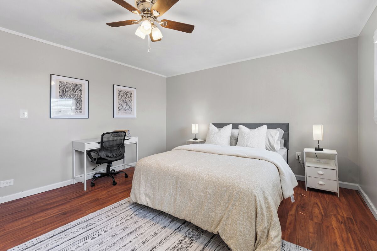 A bedroom with a bed, desk, chair, and two wall-mounted lamps.