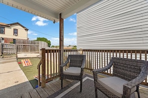 Une terrasse extérieure couverte, avec deux fauteuils en osier et un petit tapis.