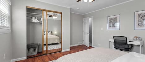 Ein Schlafzimmer mit Bett, Schreibtisch, Stuhl, Kleiderschrank und Deckenventilator.