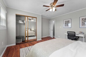 Un dormitorio con cama, escritorio, silla, armario y ventilador de techo.