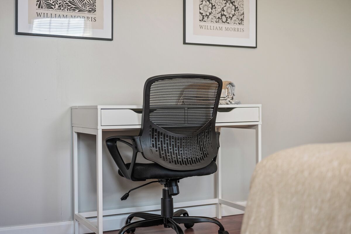 Un espace de travail comprenant un fauteuil de bureau noir, un bureau blanc et deux tableaux encadrés accrochés au mur.