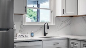 A kitchen with white cabinets, a marble backsplash, a window, and a coffee bar setup. - Mt Washington Retreat w Dedicated Parking Pets OK (Pittsburgh)