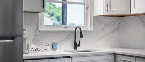 A kitchen with white cabinets, a marble backsplash, a window, and a coffee bar setup.