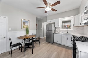 Une cuisine moderne avec des armoires blanches, un réfrigérateur en acier inoxydable, une cuisinière à gaz et un ventilateur de plafond.