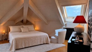 A bedroom with a sloped ceiling, a bed, bedside lamps, a nightstand, a chair, and a window. - Ponte degli Alpini | Luxury Penthouse · Sauna, 2 Hot Tubs & Panoramic Terrace (Bassano del Grappa)