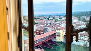 A view through a window of a cityscape with buildings, a bridge, and a river. - Ponte degli Alpini | Luxury Penthouse · Sauna, 2 Hot Tubs & Panoramic Terrace (Bassano del Grappa)