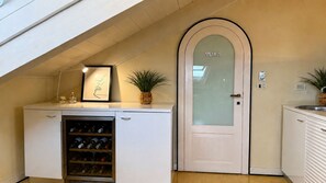 Eine kompakte Küche mit Weinkühlschrank, einer Tür mit Milchglas und einem kleinen Topf mit Pflanze.