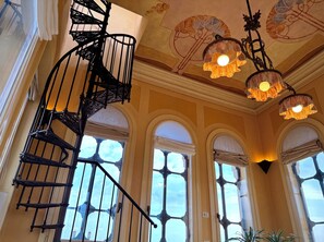 A spiral staircase with ornate railings, large arched windows with curtains, and decorative ceiling artwork. - Ponte degli Alpini | Luxury Penthouse · Sauna, 2 Hot Tubs & Panoramic Terrace (Bassano del Grappa)