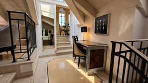 A staircase leading to a dining area with a table and chairs, a lamp, and a framed artwork on the wall. - Ponte degli Alpini | Luxury Penthouse · Sauna, 2 Hot Tubs & Panoramic Terrace (Bassano del Grappa)