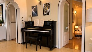 Ein Klavier in einem Raum mit einer Tür, einer Vase und einem gerahmten Bild an der Wand.