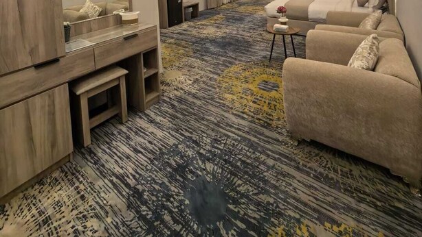 A modern hotel room with a sofa, a small table, a mirror, and a patterned carpet.