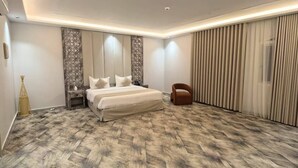 A bedroom with a large bed, a nightstand, a chair, and a window with curtains.