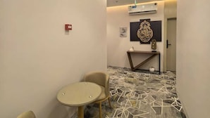 A hotel corridor with a round table and two chairs, a decorative wall piece, and an air conditioning unit.
