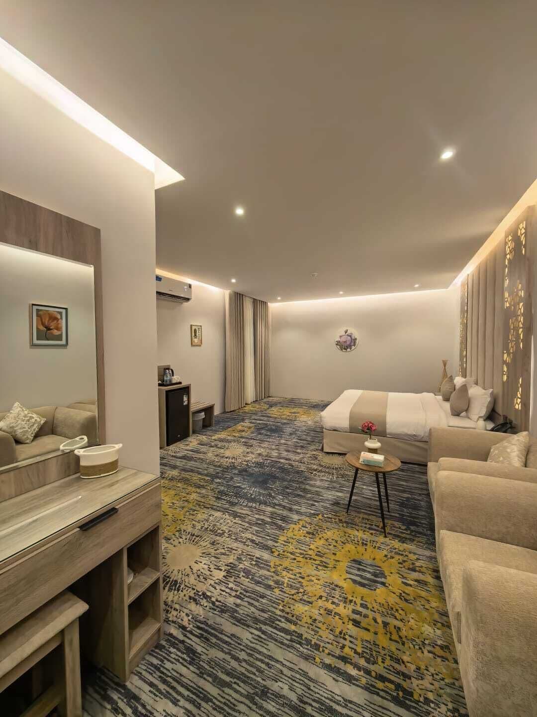 A modern hotel room with a large bed, a sofa, a small table, and a built-in TV.