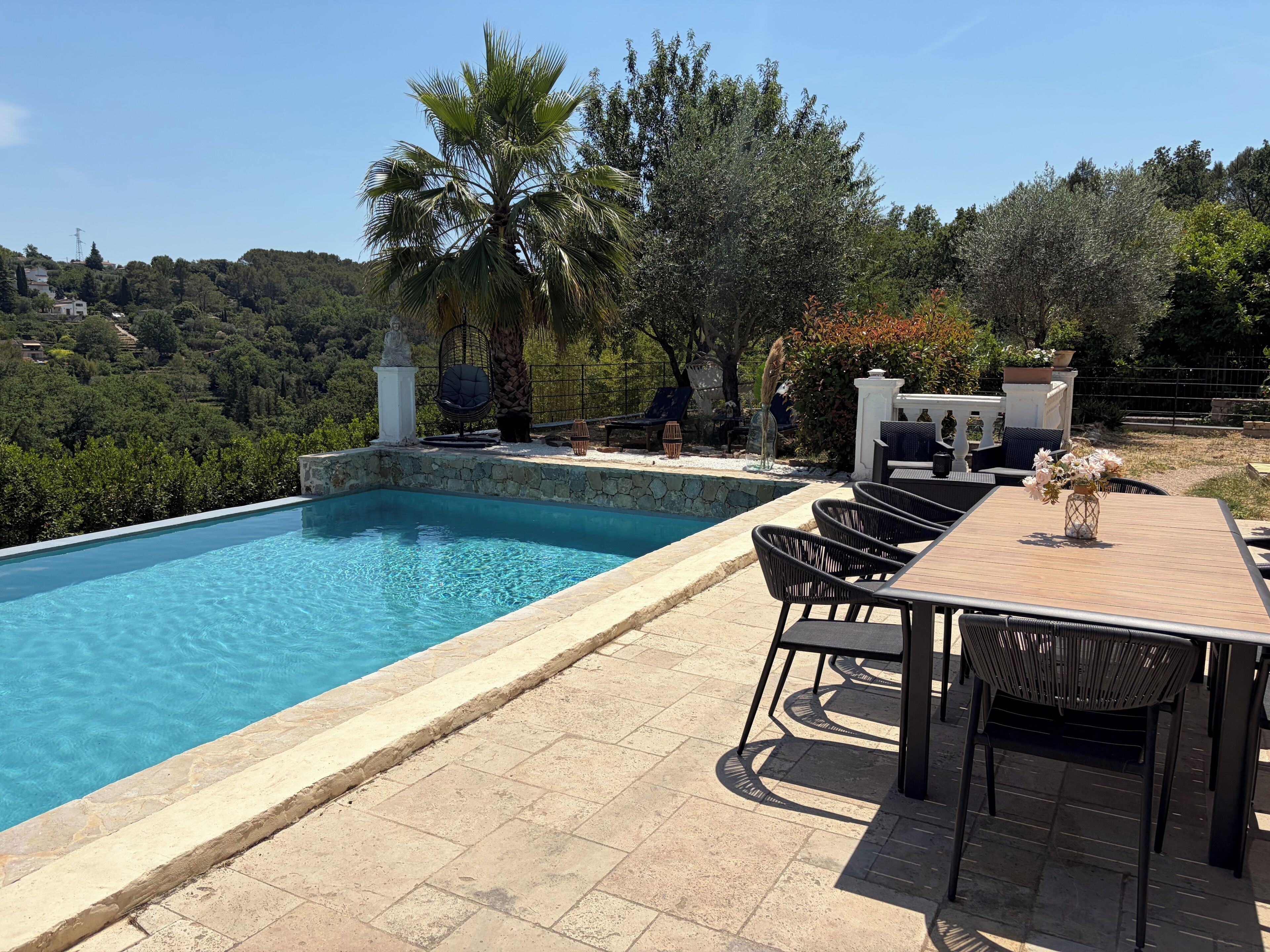 A pool with a stone border, outdoor furniture, and a view of the surrounding landscape.