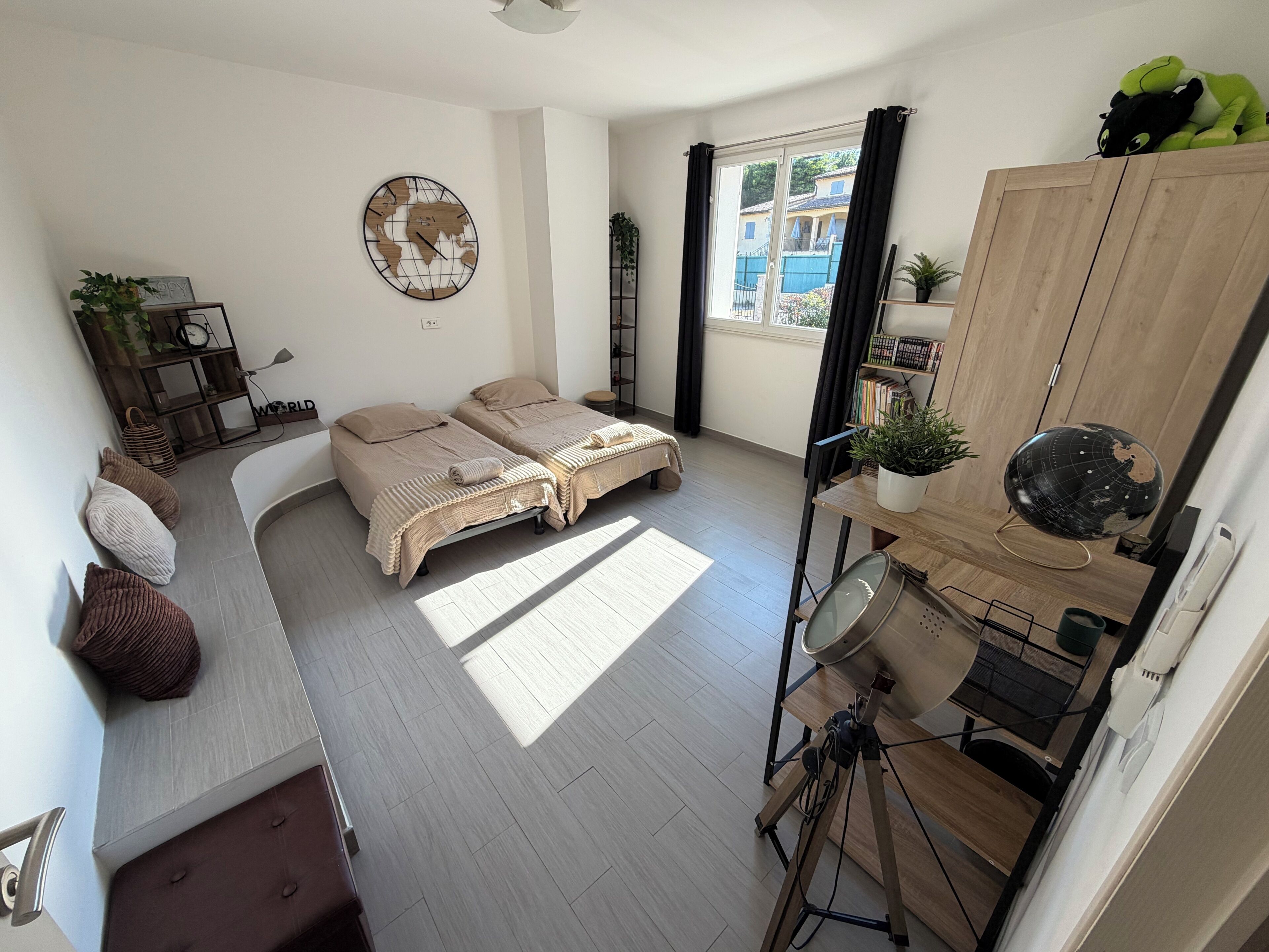 A modern bedroom with two beds, a globe wall art, a wooden cabinet, and a desk with a globe and plant.