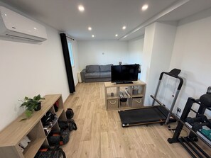 A modern living space with a grey sofa, a flat-screen TV, a treadmill, and a shoe rack. - Large villa with a large pool and a gym (Grasse)
