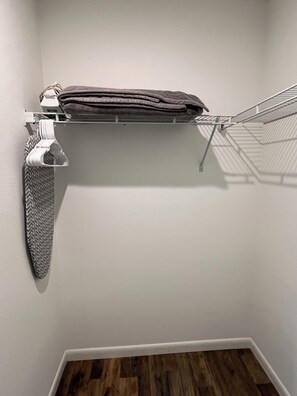 A corner of a room with a white wall, a wooden floor, a metal drying rack, and a towel rack with folded towels and a patterned tie. - Cozy Tampa Home 2BR, 2BA & Fenced Yard (Tampa)