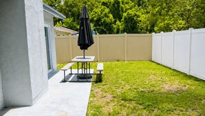 Un jardin avec une table de patio, un banc et un parasol.