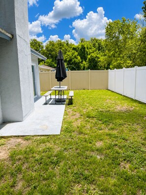 A backyard with a patio table, a bench, and an umbrella. - Cozy Tampa Home (Tampa)