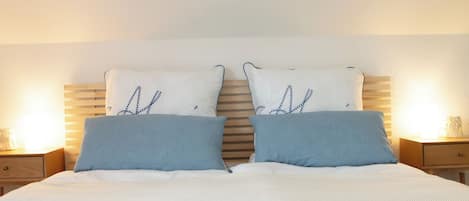 Una cama con cabecera de madera, dos almohadas con estampado de hojas y una colcha con diseño de ancla náutica.