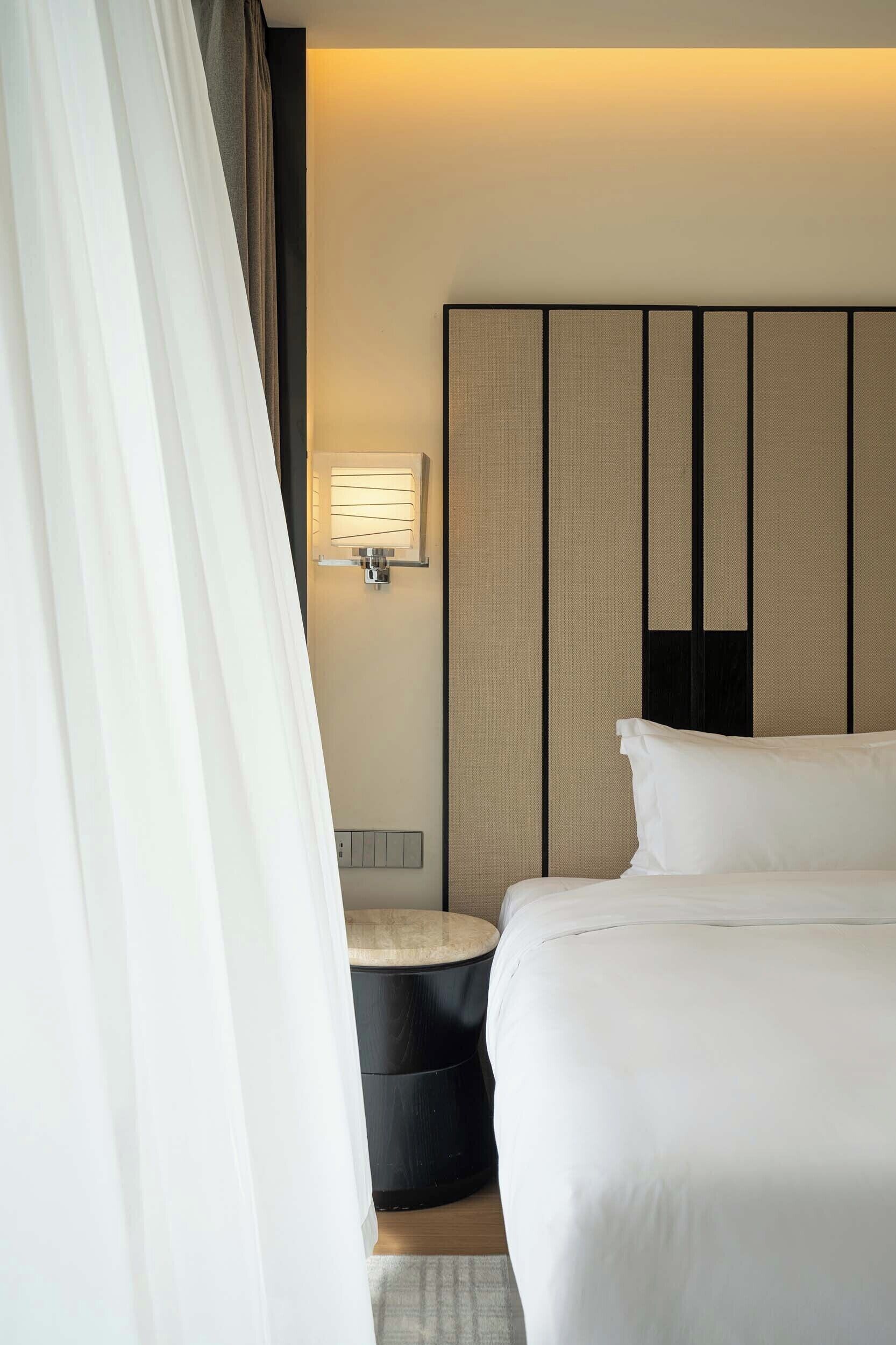 Habitación de hotel con cama, mesita de noche, luz en la pared y cortina.