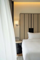 Habitación de hotel con cama, mesita de noche, luz en la pared y cortina.