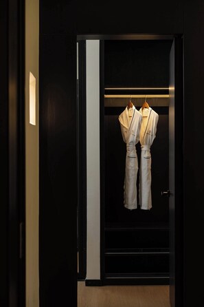 Una habitación oscura con una puerta de madera, un accesorio de iluminación y dos batas blancas colgadas en un perchero.