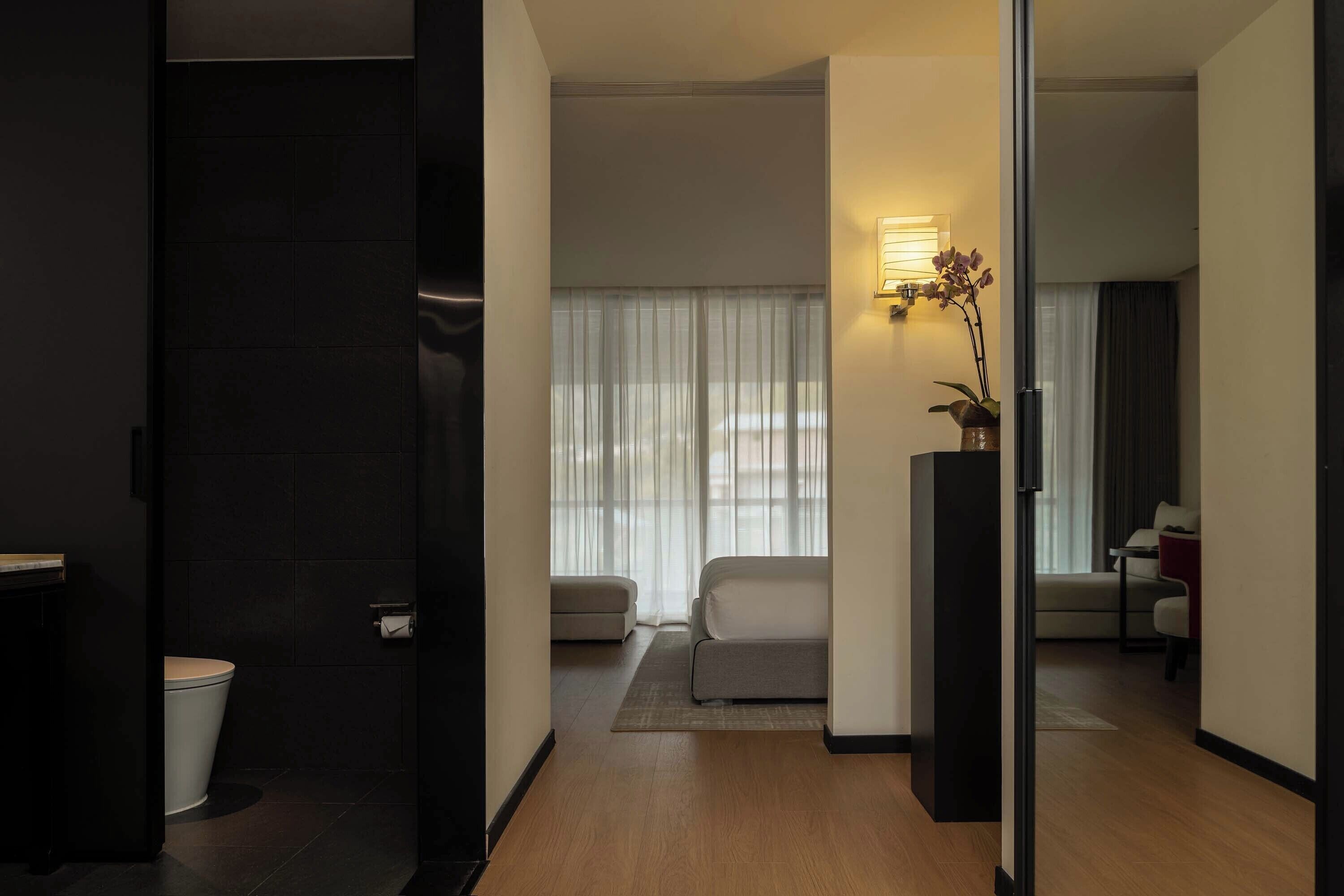 Ein modernes Hotelzimmer mit Holzboden, einer Couch, einem kleinen Tisch und einer Topfpflanze.