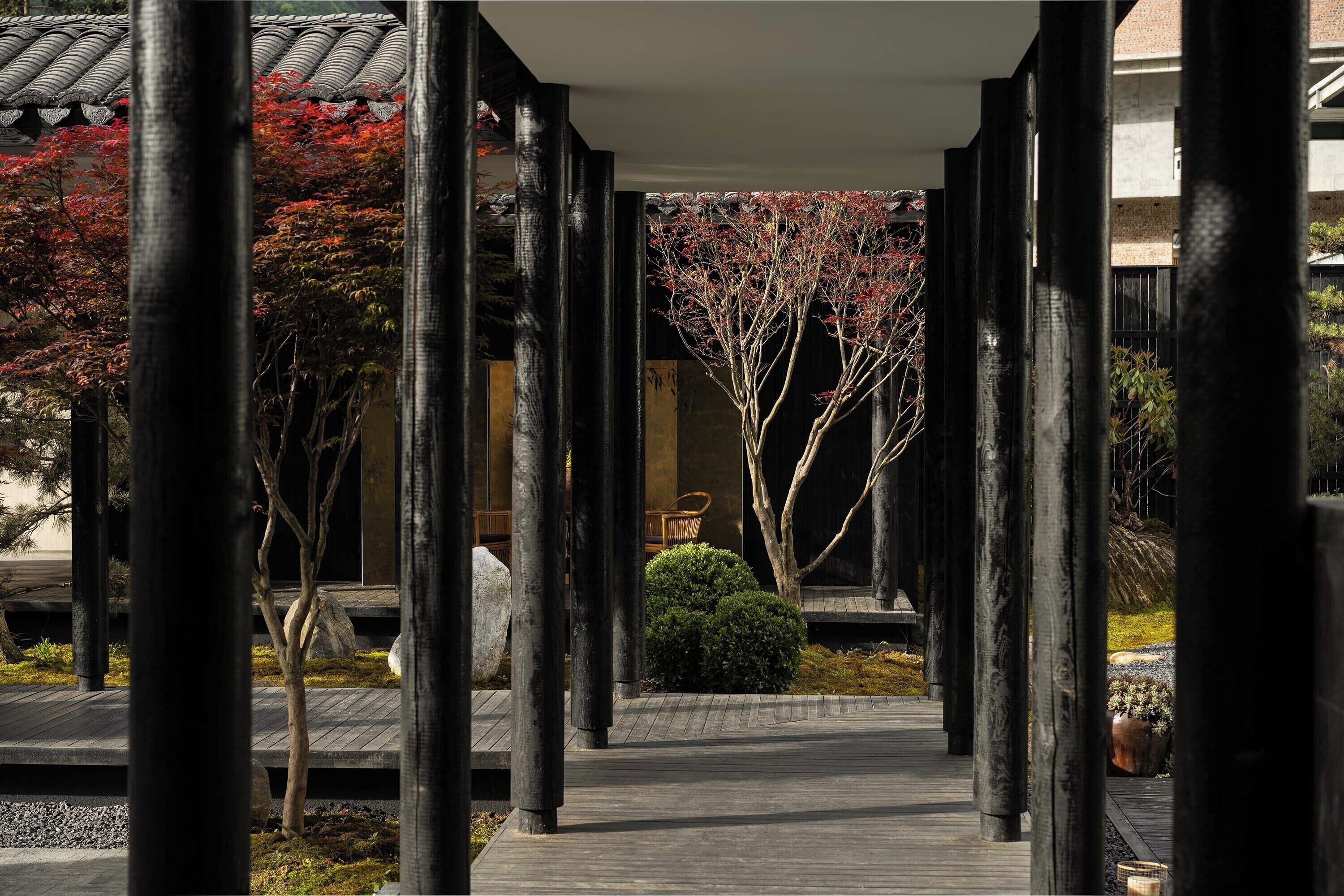 Un corredor tradicional al estilo japonés con pilares de madera, techo de tejas y un sendero que lleva a un edificio.