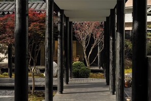 Un couloir de style japonais traditionnel, avec des piliers en bois, un toit recouvert de tuiles et un chemin menant à un bâtiment.