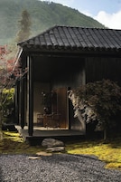 Un edificio japonés tradicional con tejado de tejas, un porche de madera y un jardín con rocas y plantas.