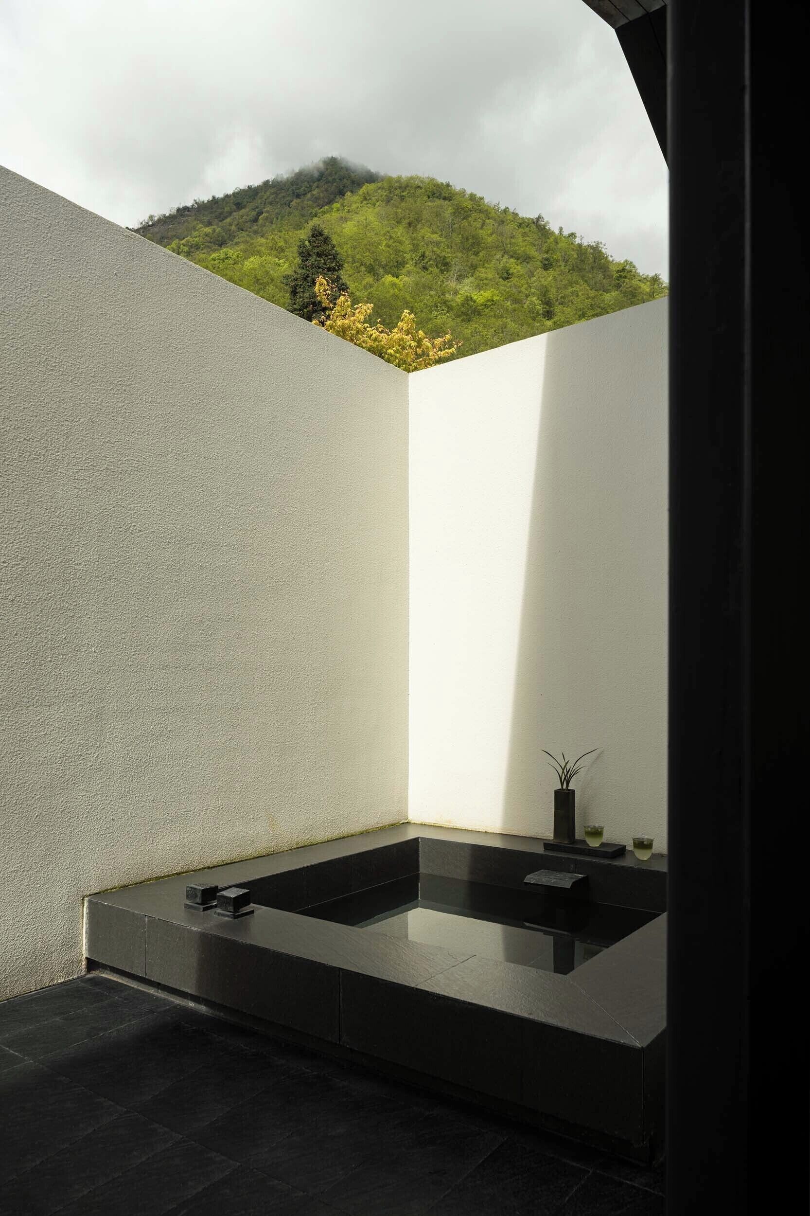 A modern bathroom with a large bathtub, a small sink, and a potted plant.