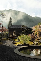 Una casa tradicional japonesa con jardín, estanque y montañas al fondo.