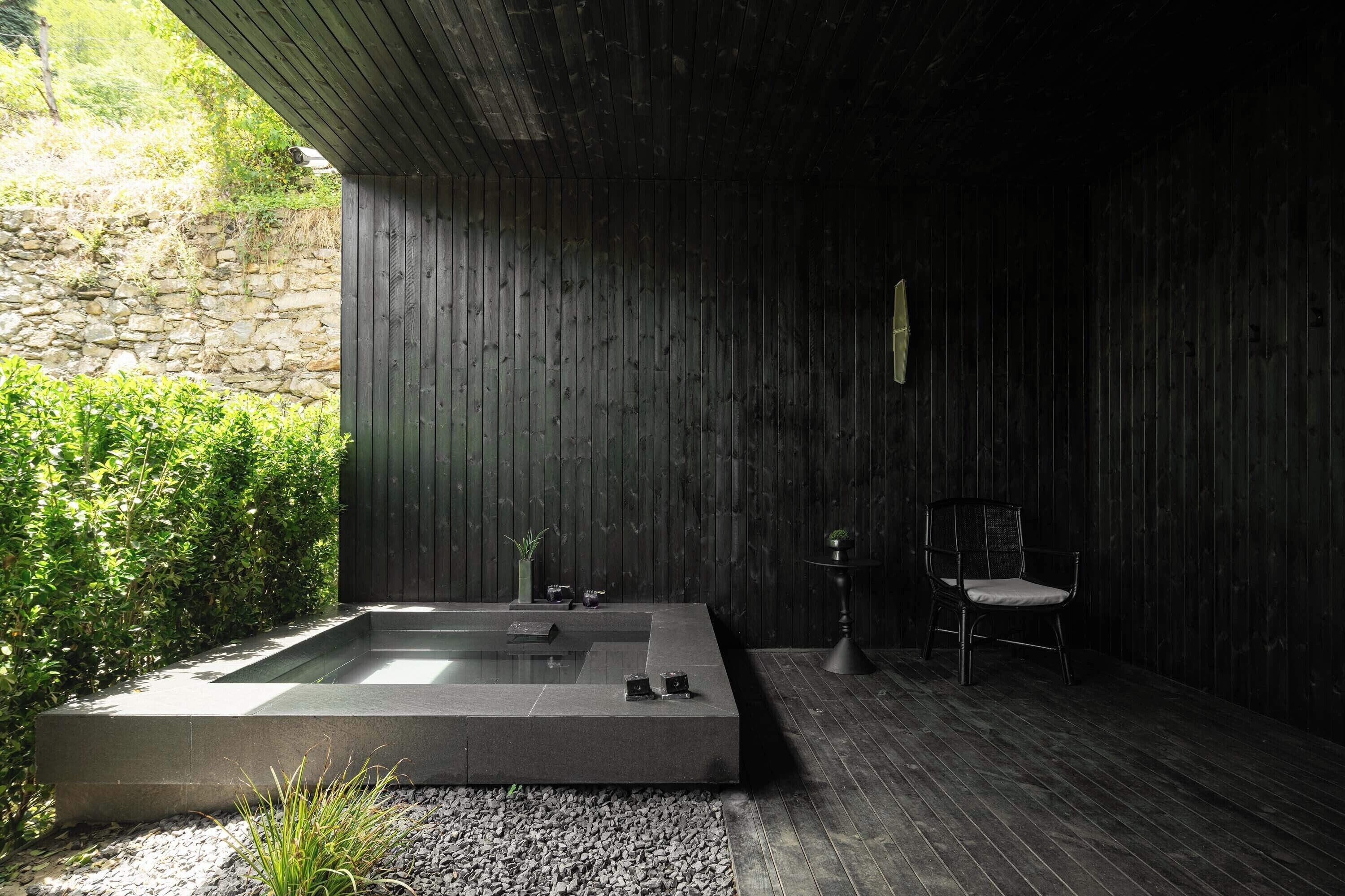 A modern spa room with a rectangular hot tub, a chair, and a small table.