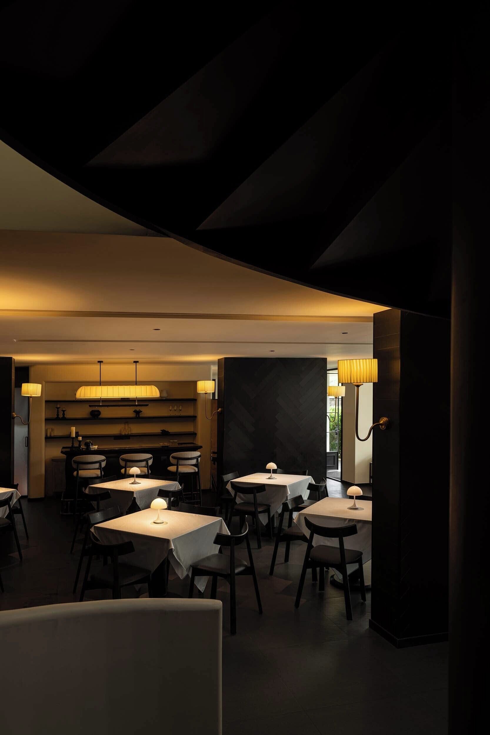 A dimly lit restaurant with tables and chairs, a bar area, and pendant lighting.