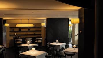 A dimly lit restaurant with tables and chairs, a bar area, and pendant lighting.