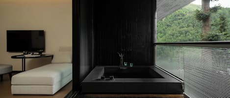 Un baño moderno con una bañera grande, un televisor de pantalla plana y vistas a un bosque.