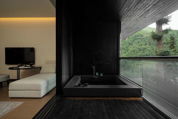 A modern bathroom with a large bathtub, a flat-screen TV, and a view of a forest.