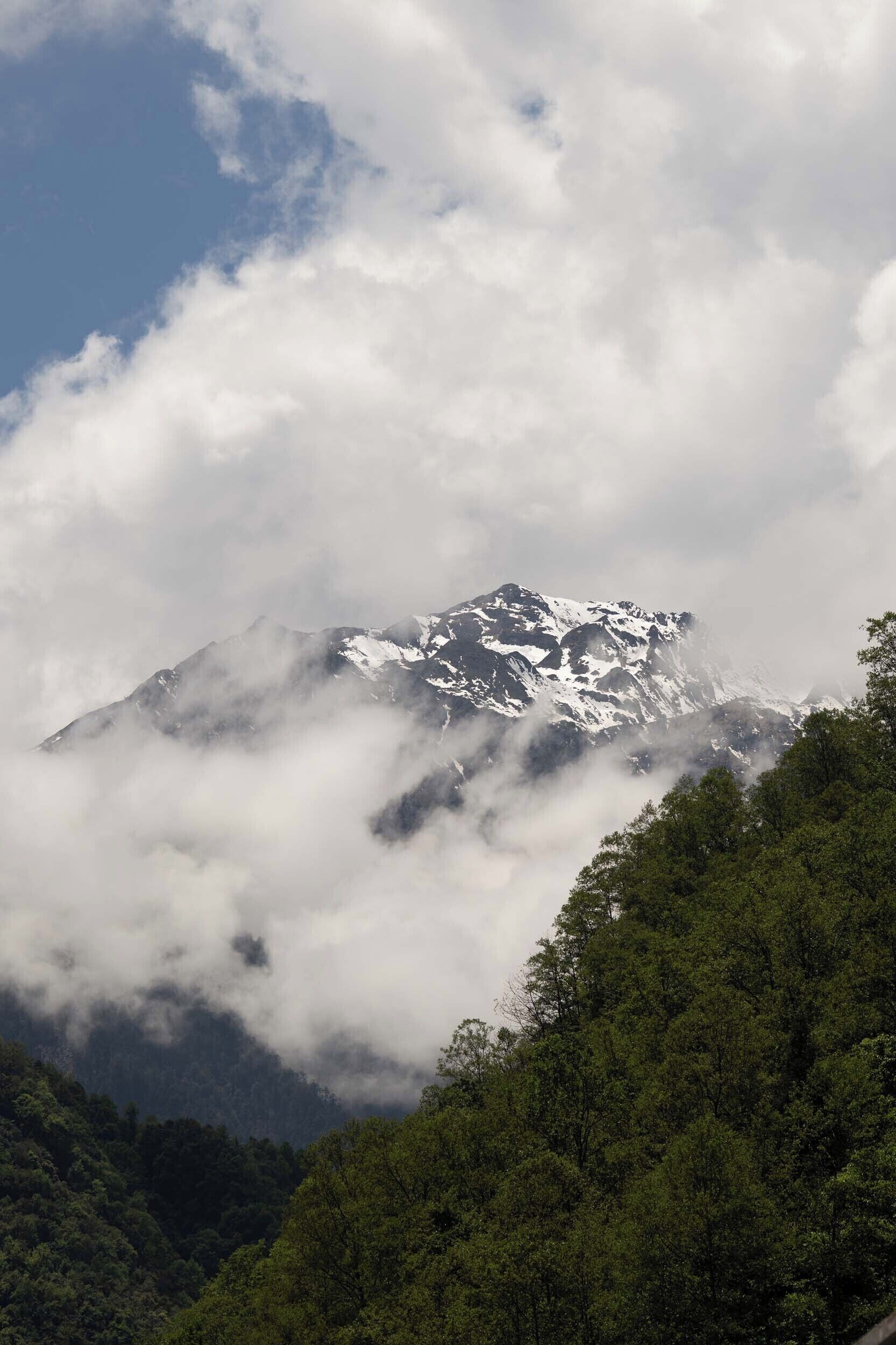 Une montagne dont les sommets enneigés sont partiellement cachés par les nuages.