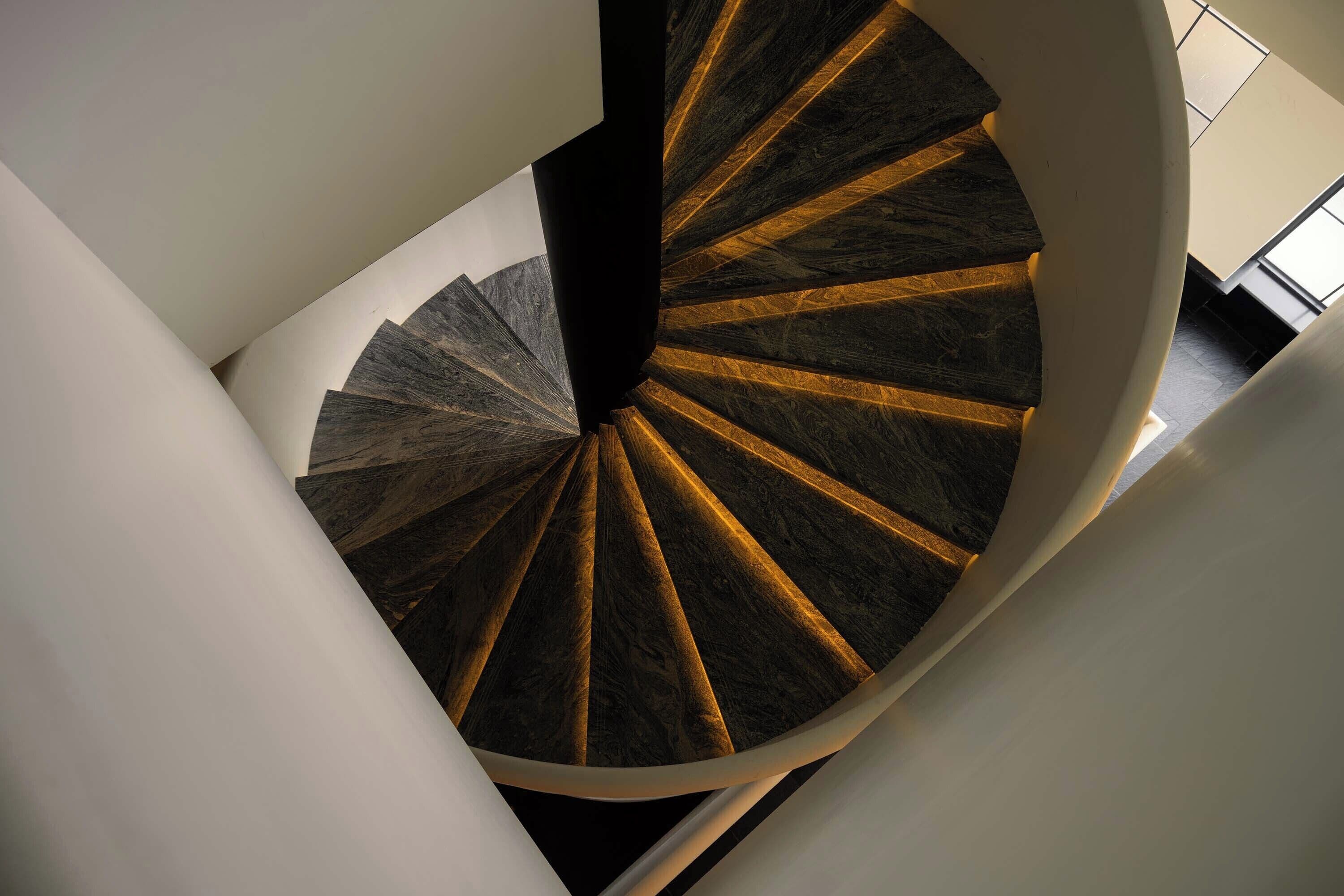 A spiral staircase with a dark, patterned floor and white walls.